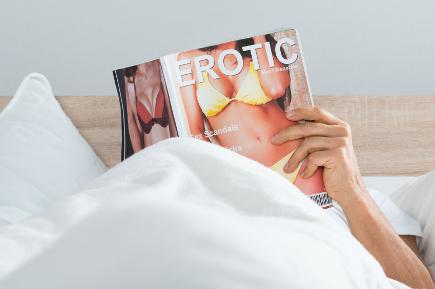 Close-up Of A Man Lying On Bed Reading Erotic Magazine At Home