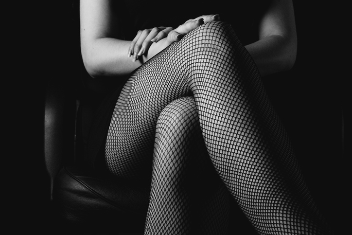 sexy woman in black fishnet stockings sitting on chair on dark